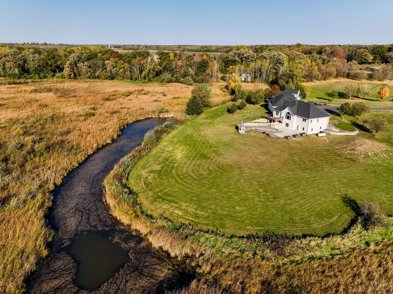 Angled aerial view of a house and lawn bordered by water and reeds.