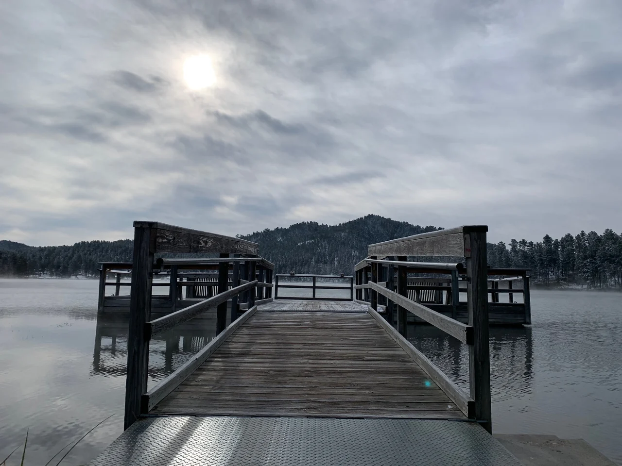 A wooden pier reaching into a lake beneath a cloudy sky.